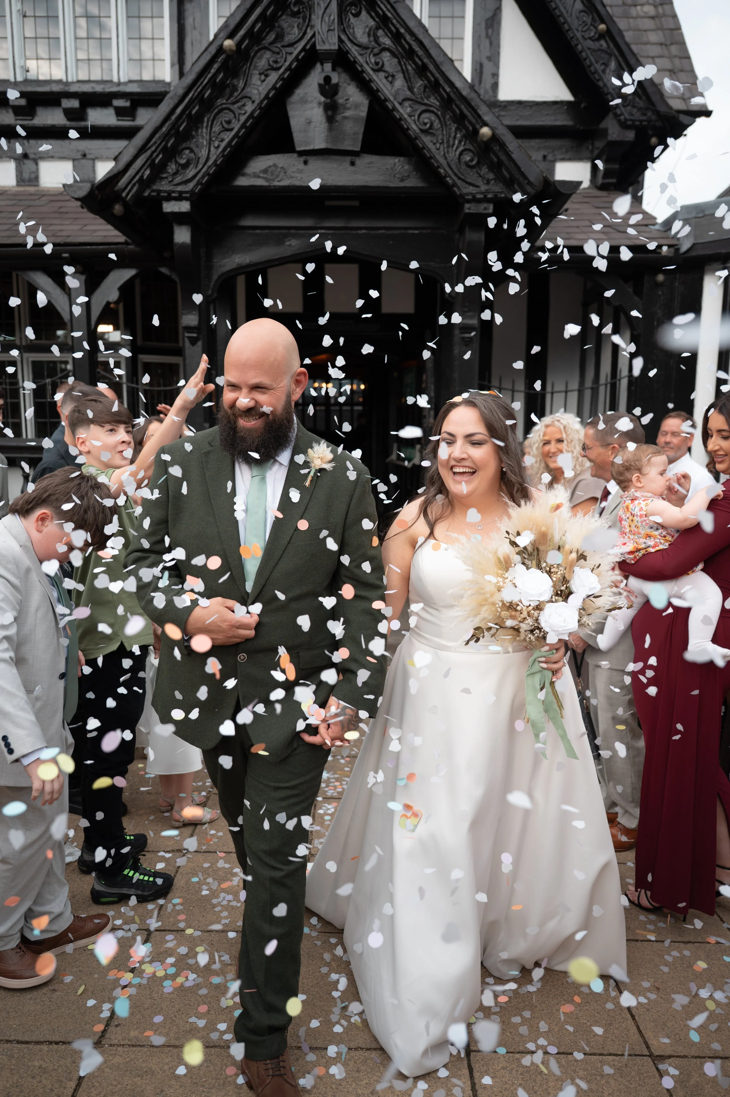 A newlywed couple walking through a shower of confetti outside a church, surrounded by friends and family celebrating their wedding.
