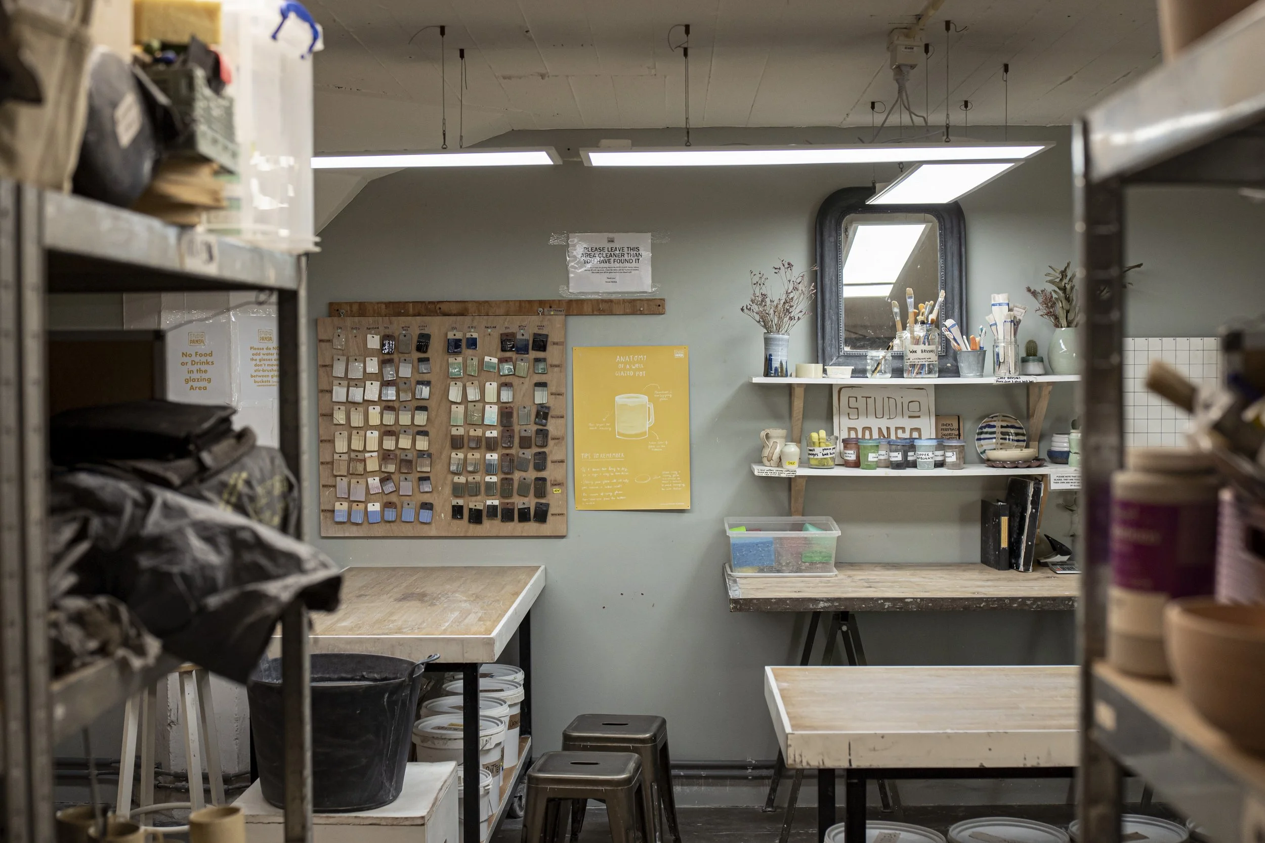 Interior of an art studio or workspace with shelves, tables, and a wall display of color swatches.
