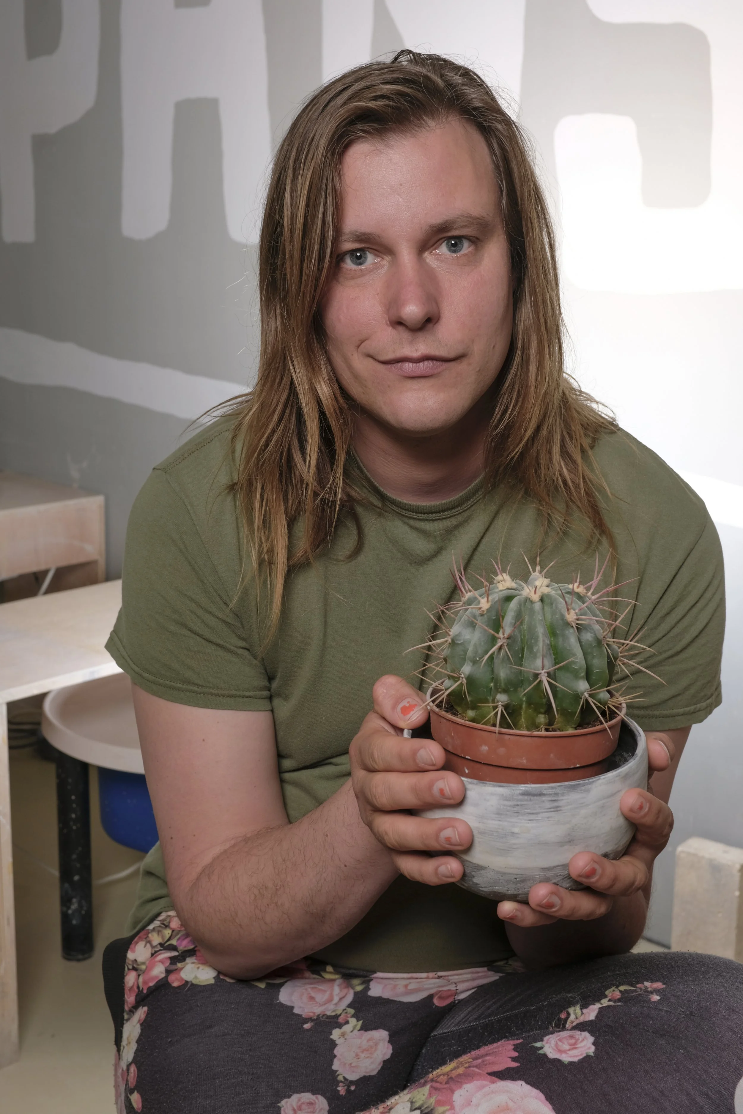 A person with long hair and a green shirt holding a potted cactus plant.
