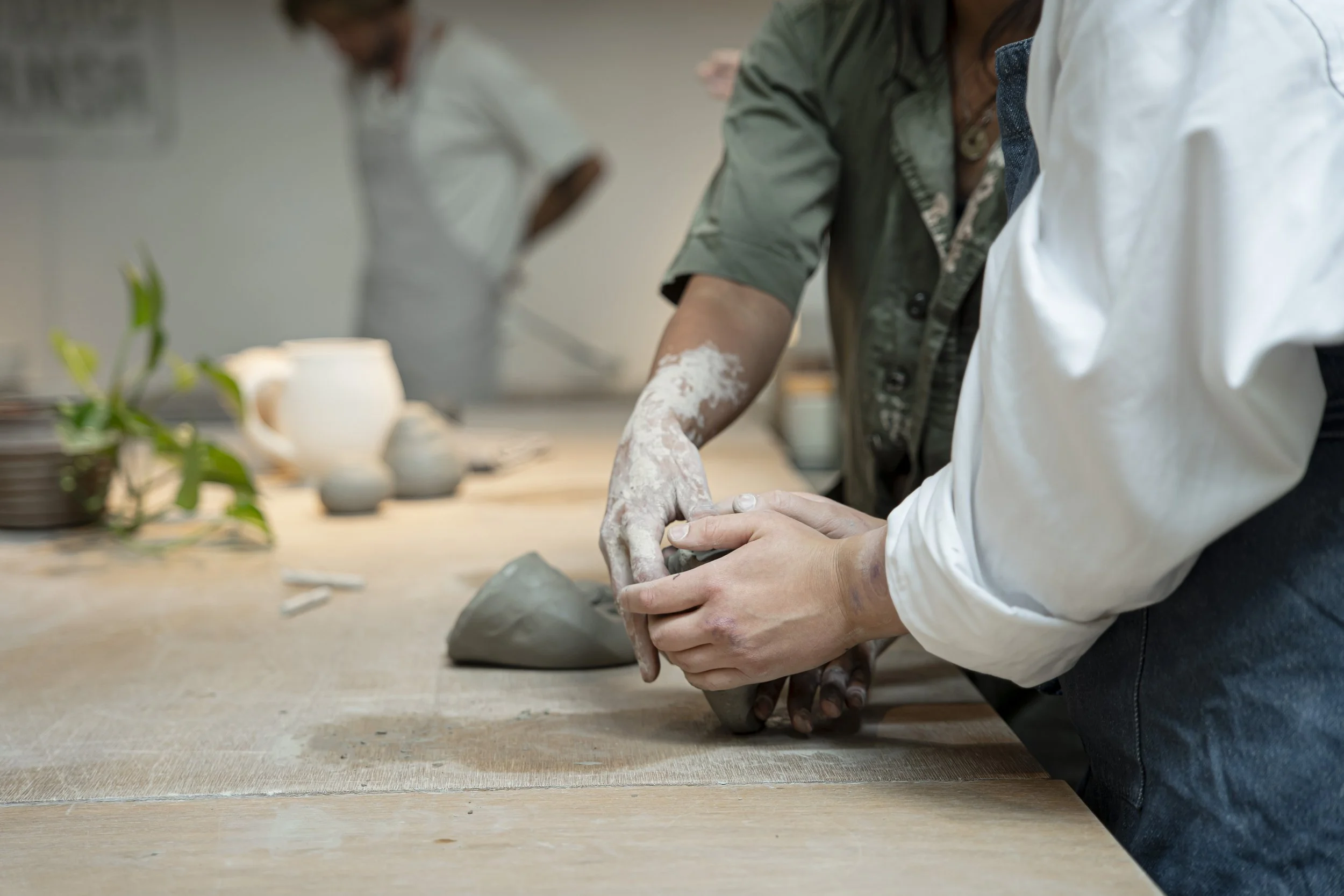 People making pottery with clay on a worktable, focusing on hands shaping the clay.