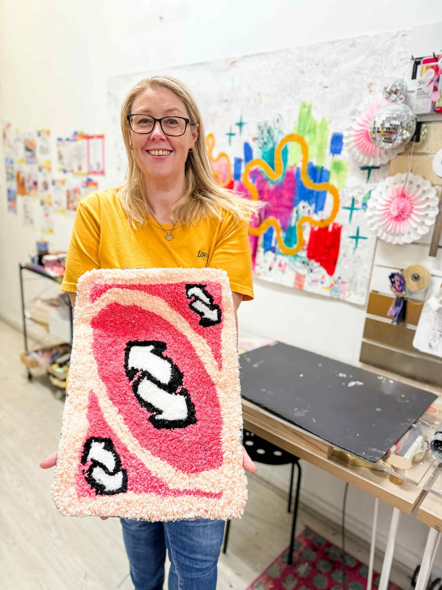 A smiling woman in a yellow t-shirt proudly holding a pink Uno tufted rug