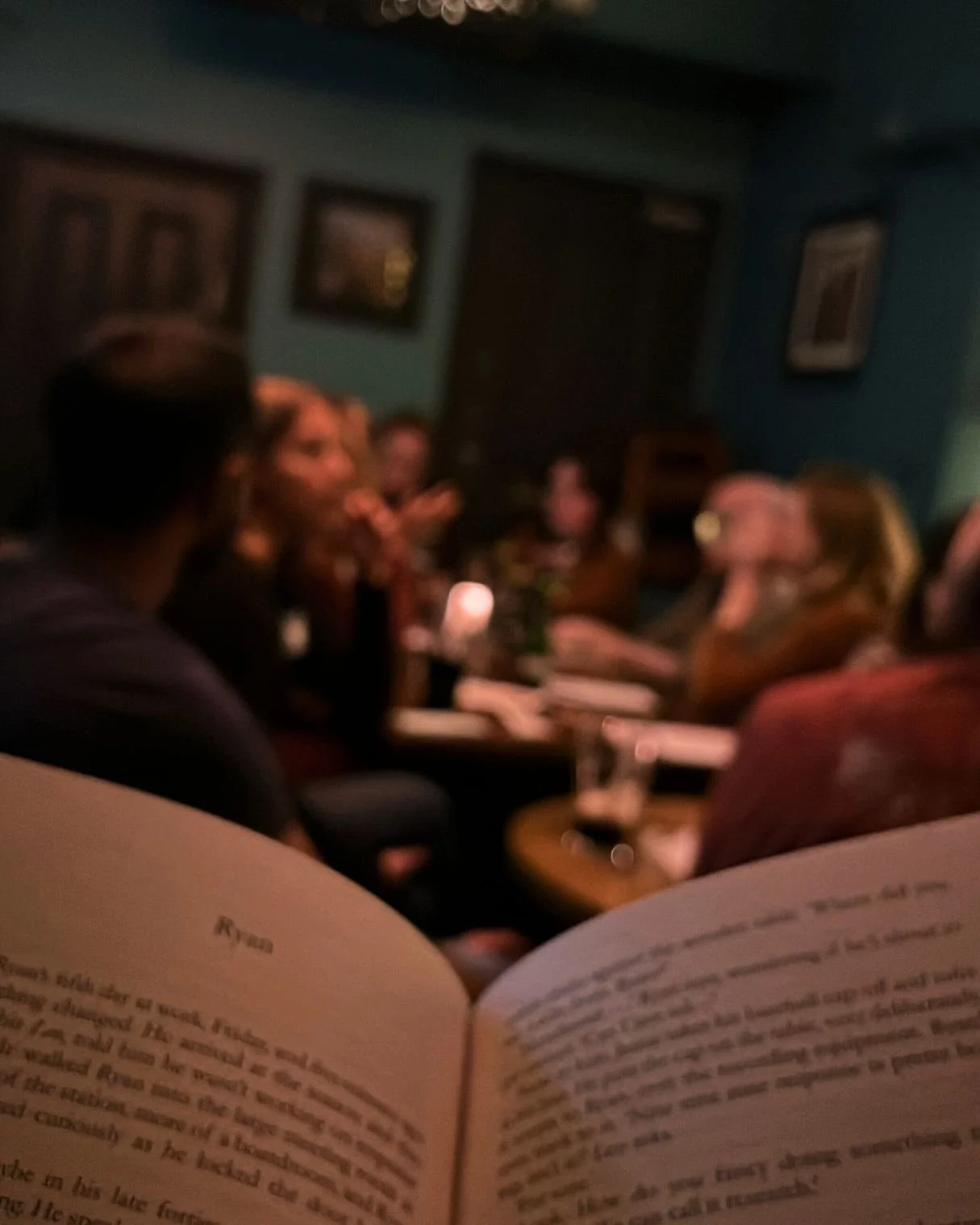 an open book with groups of people in the background sitting at tables talking