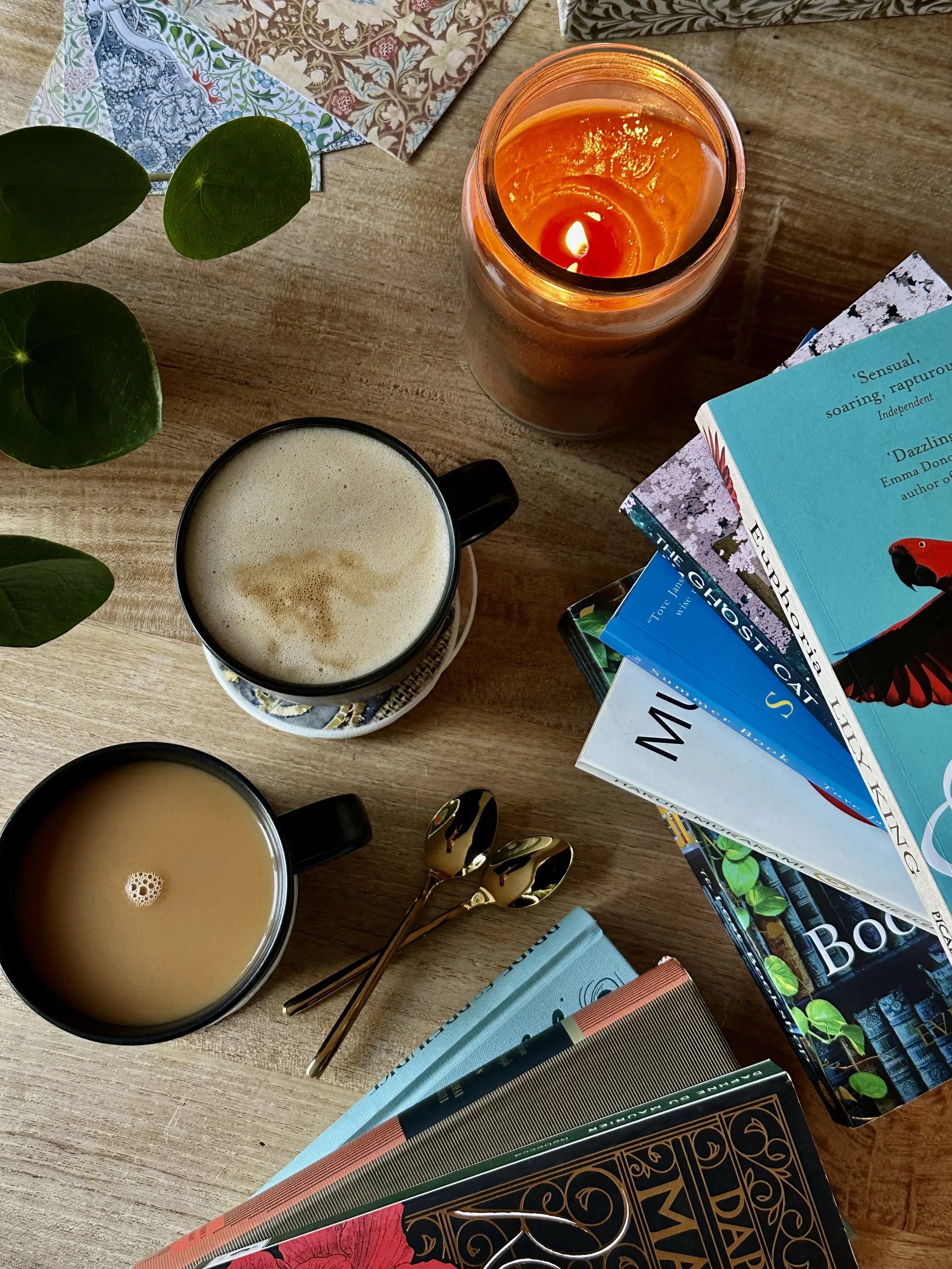view of table holding cups of coffee, tea, a candle, and pile of books.
