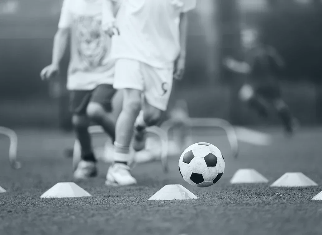 Kinder beim Fußballtraining, die über Hütchen laufen.