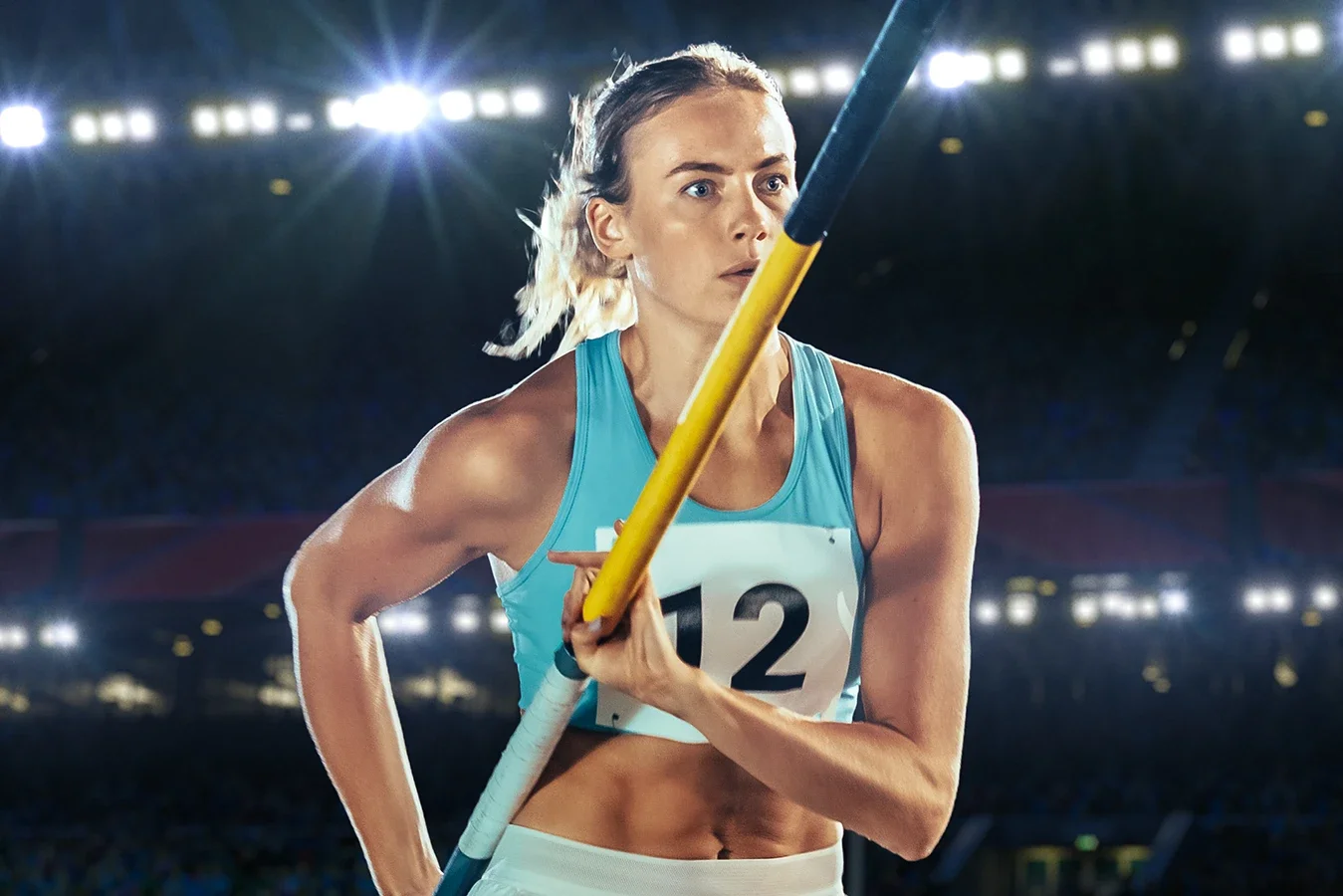 Leichtathletin mit Stab beim Speerwurf, im Stadion bei Nacht mit Lichteffekten im Hintergrund.