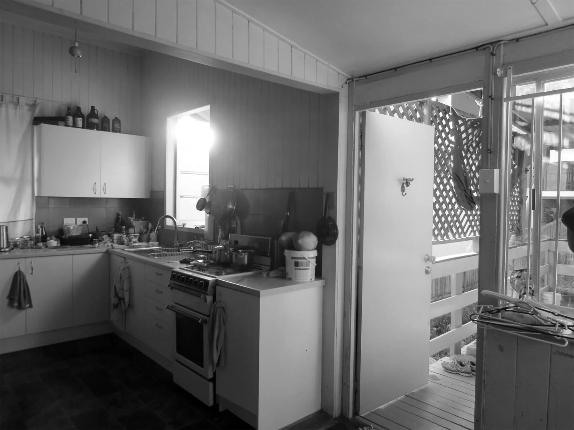 A black and white kitchen, featuring VJ paneling and a bright window, opens to a lattice-screened outdoor veranda with railings.