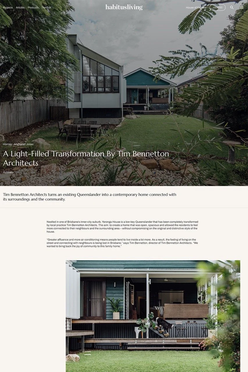 Exterior view of a modern Queenslander-style home with large windows, a small front porch, surrounded by greenery and a fenced yard.