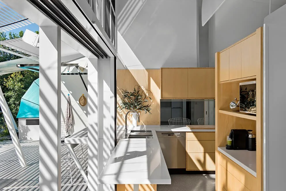 Modern kitchen with white countertops, wooden cabinets, a sink with a faucet, and a large window letting in natural light.