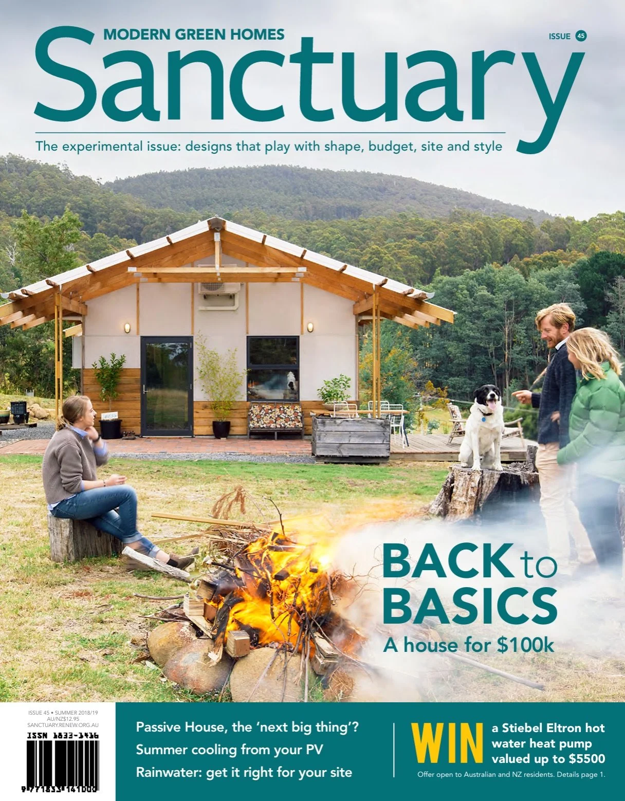 A magazine cover titled "Sanctuary" featuring a small modern green home with a wooden roof structure, people sitting around a campfire, and two dogs outdoors in a green mountain landscape.