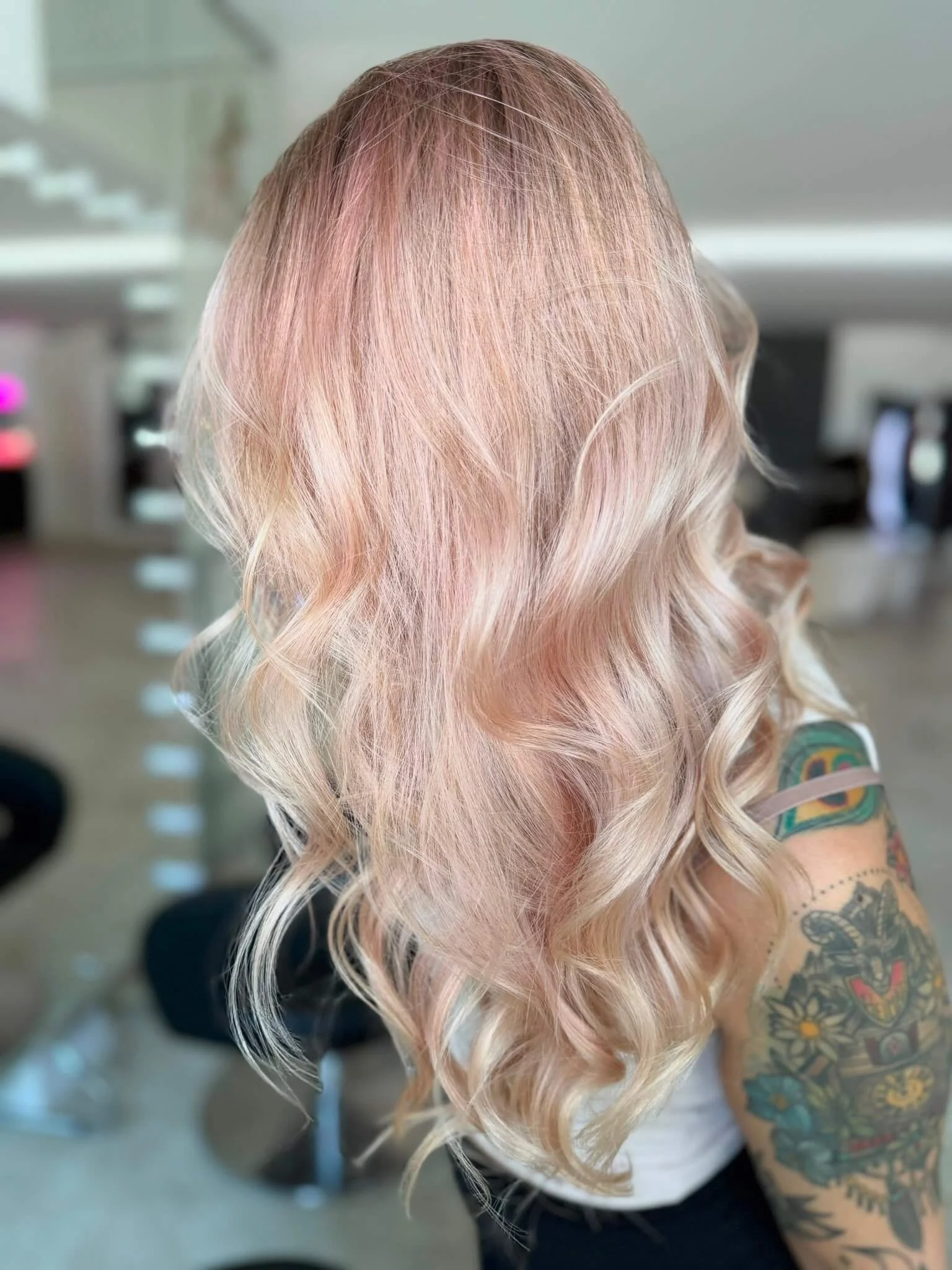 Nahaufnahme von einer Frau mit langen, lockigen, pastell rosa und blonden Haaren, sichtbar ist ihr arm mit einem Tattoo.