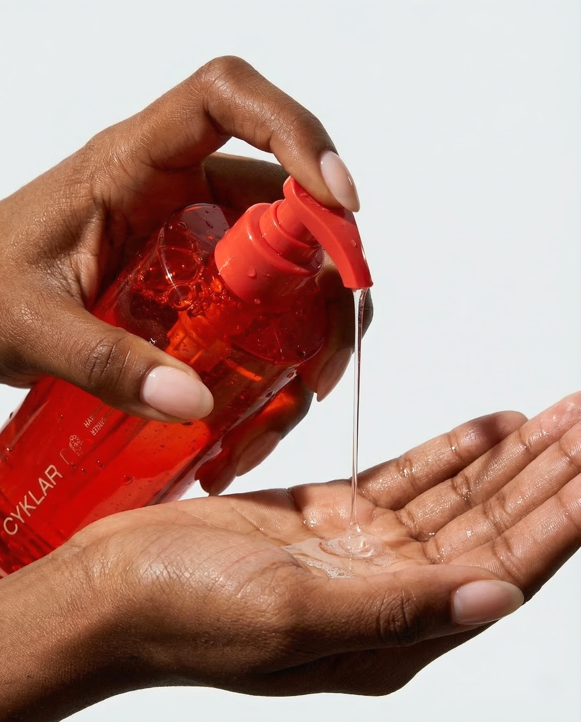 Person dispensing liquid soap onto another hand, white background.