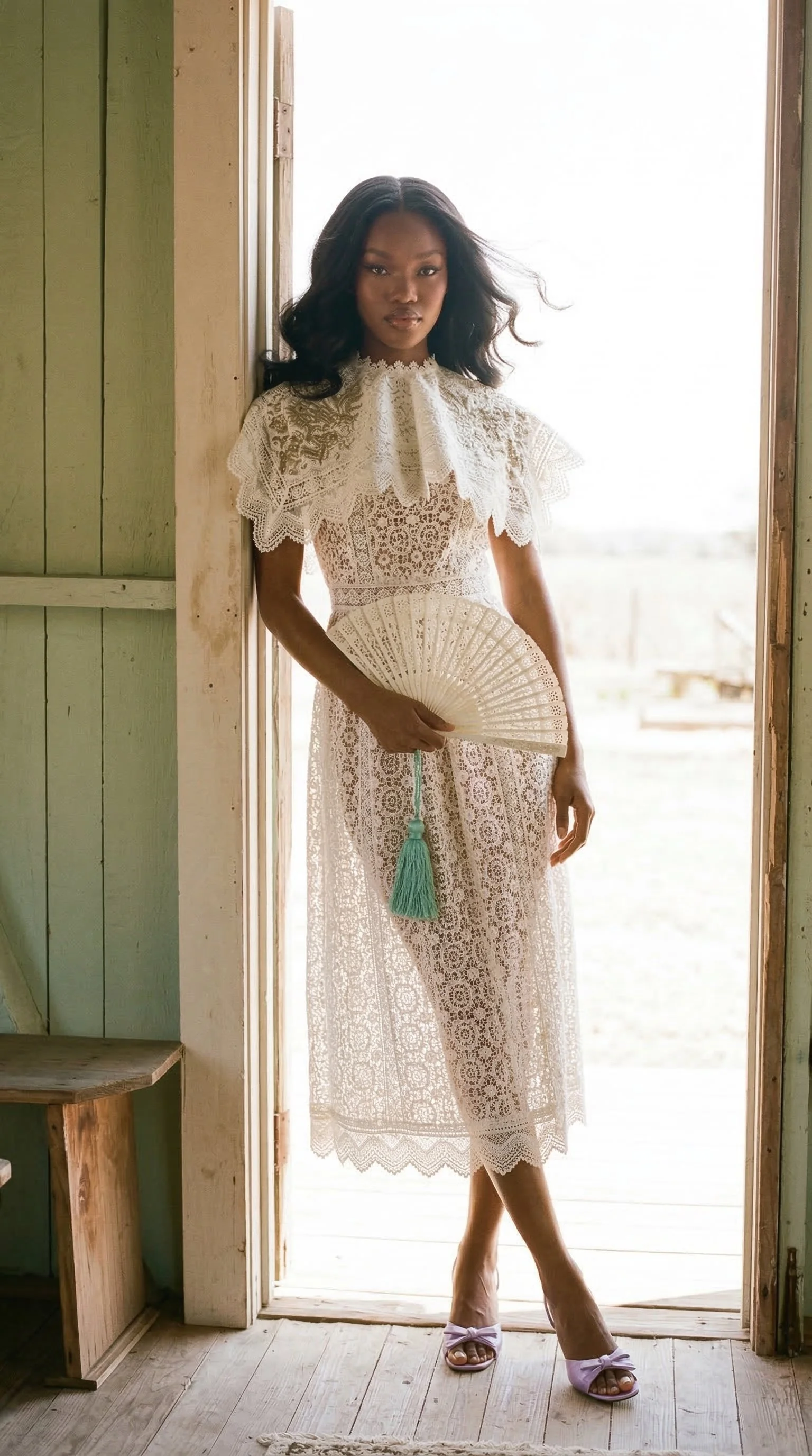 A woman standing in a doorway wearing a white lace dress, holding a folding fan, with natural light illuminating her from behind. Studio Abdul ai campaign image 