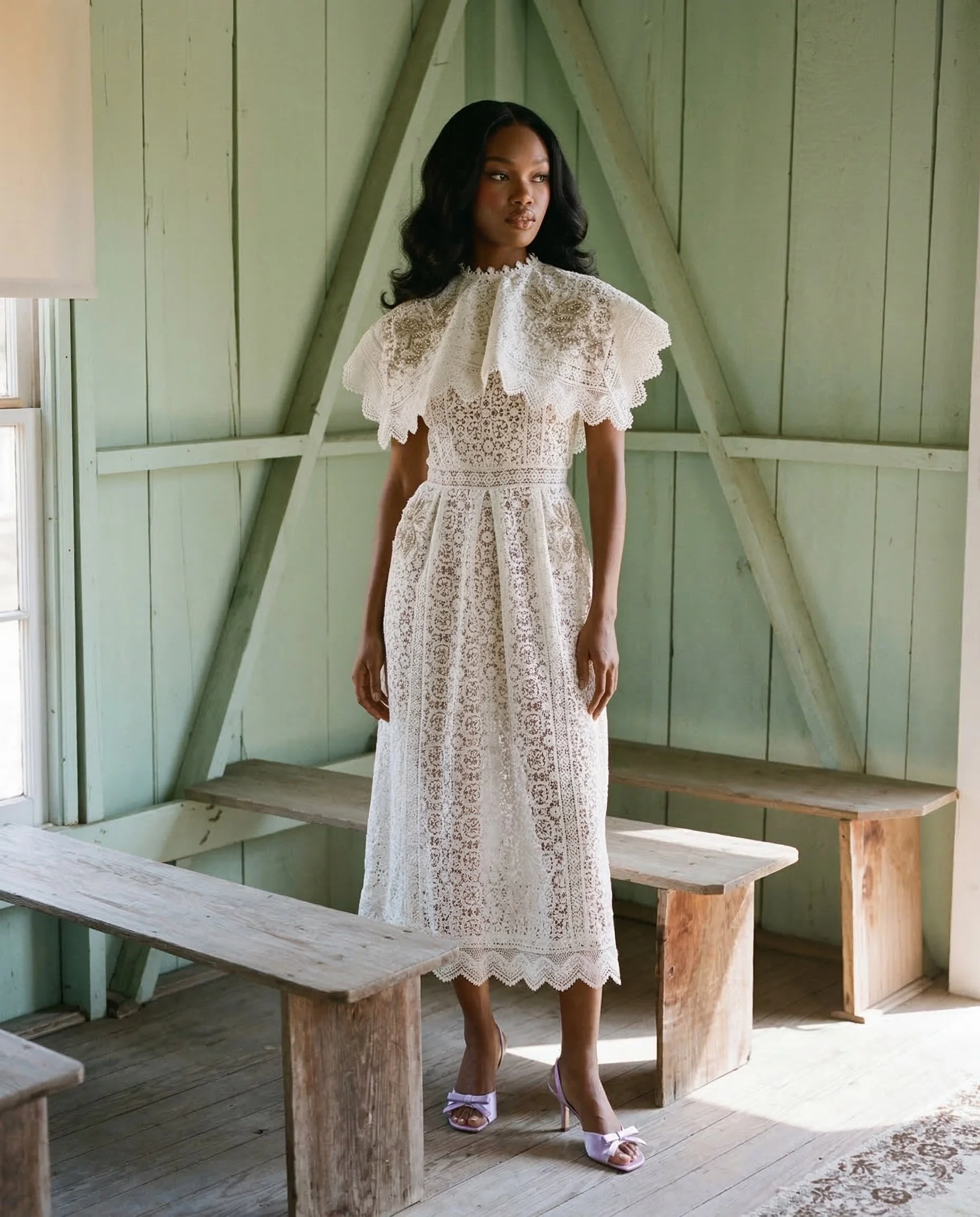 A woman in a vintage white lace dress with ruffled collar, standing inside a rustic green wooden room with benches. Studio Abdul ai campaign image 