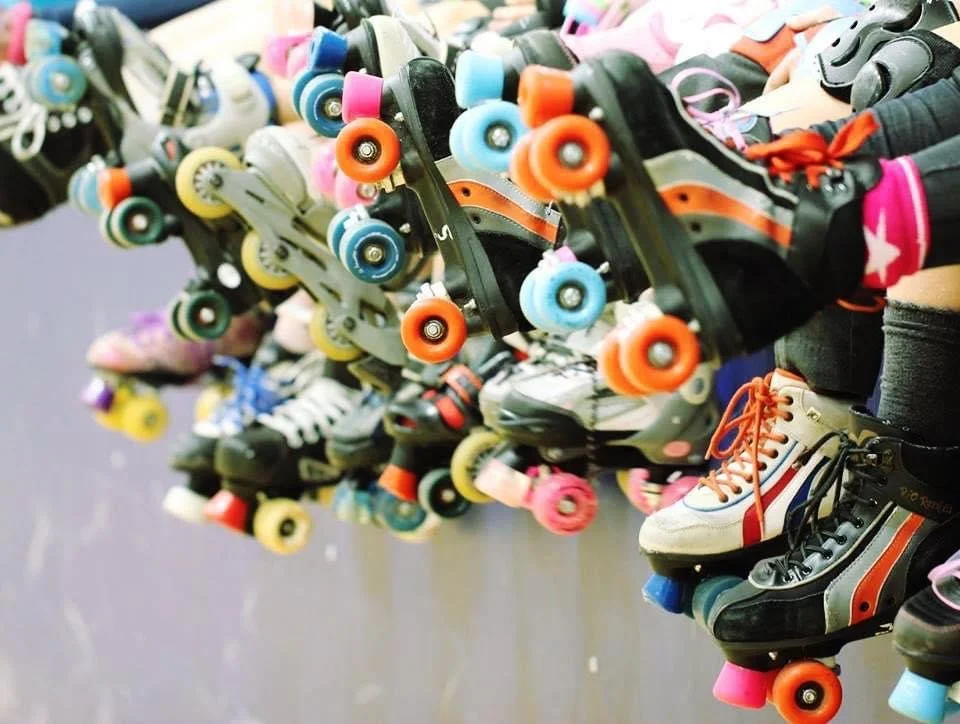 Multiple pairs of roller skates and inline skates lined up on a bench.