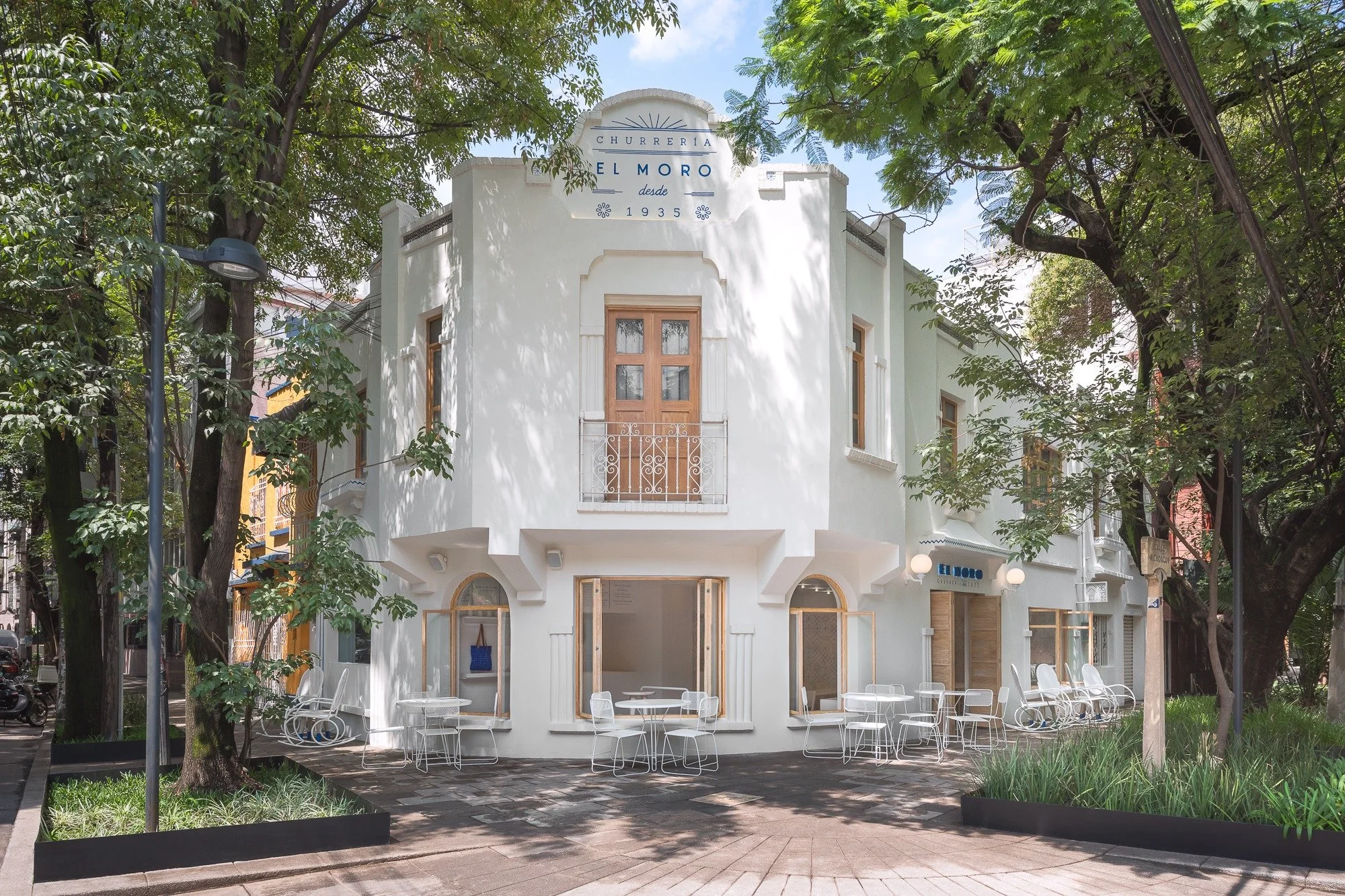 White two-story building with outdoor seating, surrounded by trees, with signs indicating it is a restaurant named 'El Moro' established in 1935, in La Condesa Neighbourhood, Mexico City.