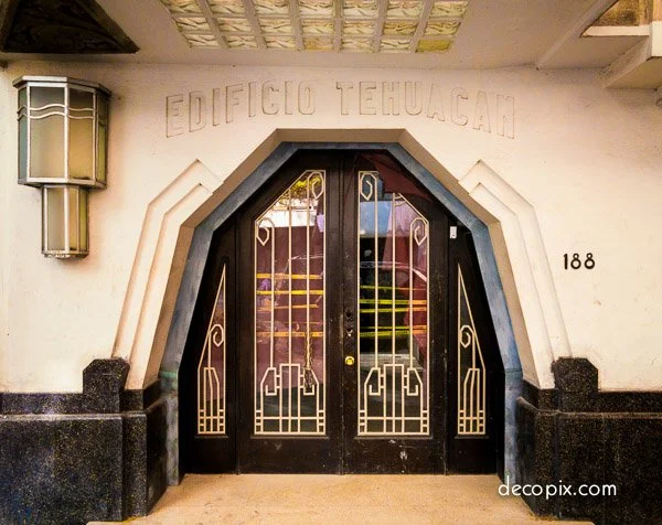 Entrance to Edificio Tehuacan with black iron door and geometric design, arched doorway, decorative wall lights, and the building number 188.