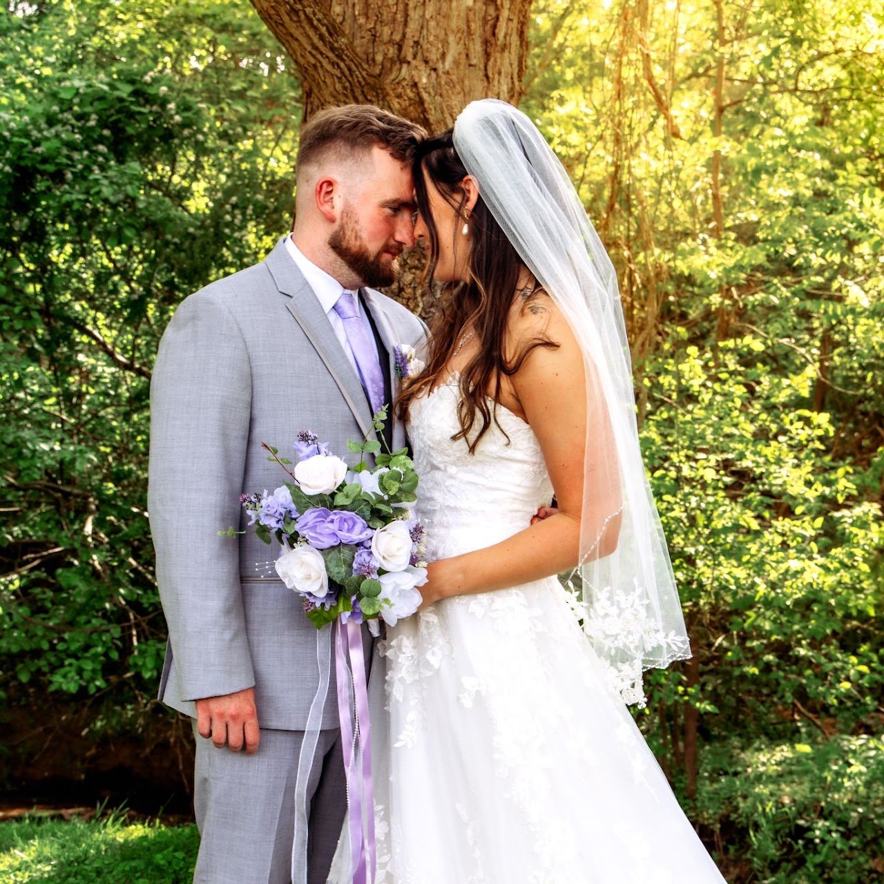 A husband and bride pose next to a tree.