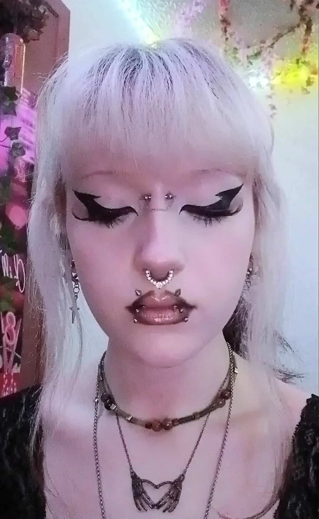 A woman with her eyes closed. She has several facial piercings, including a septum, angel fangs, snake bites, and a bridge.