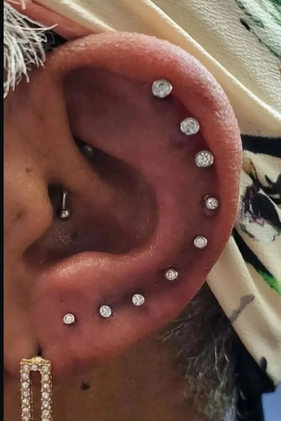 An up-close photo of an ear with a formation of 9 piercings going down along the outer curve of her ear. 
