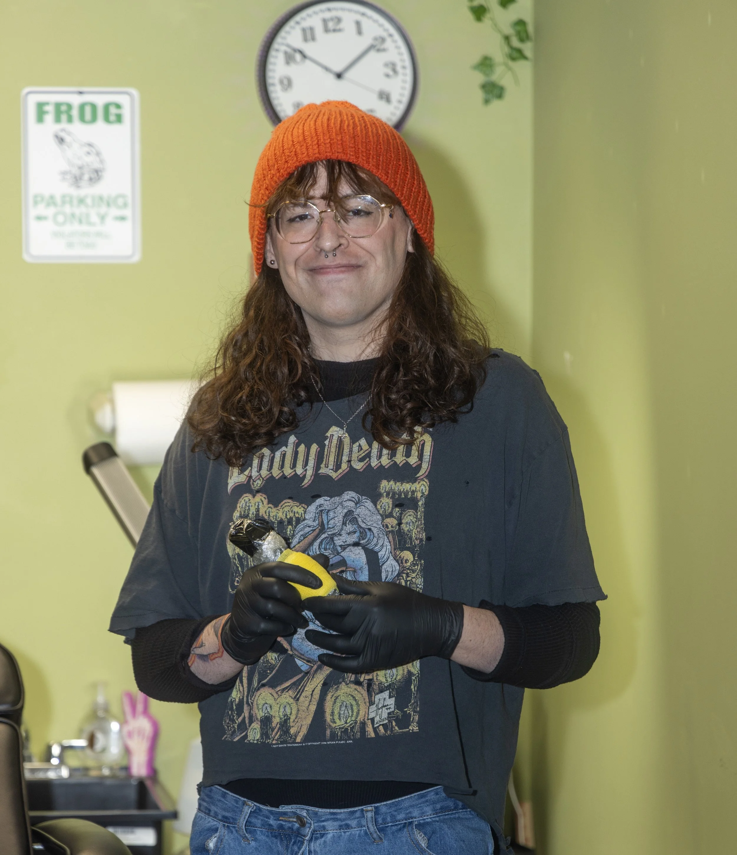 B.A. Miller smiles while standing in a tattoo studio and holding a tattoo machine.