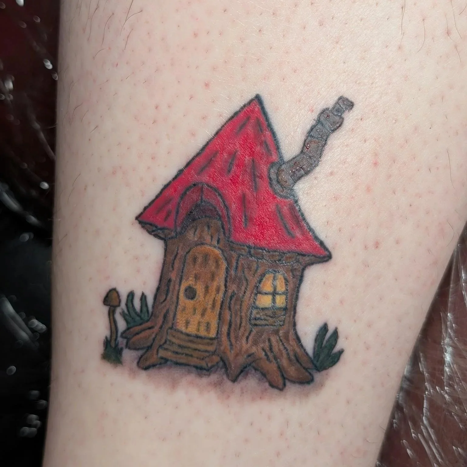 A tattoo of a small house made from a tree stump.