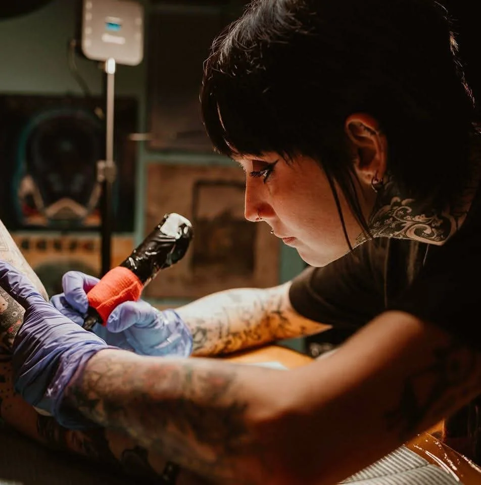 An up-close photo of Caitlin as focuses as she tattoos a client.