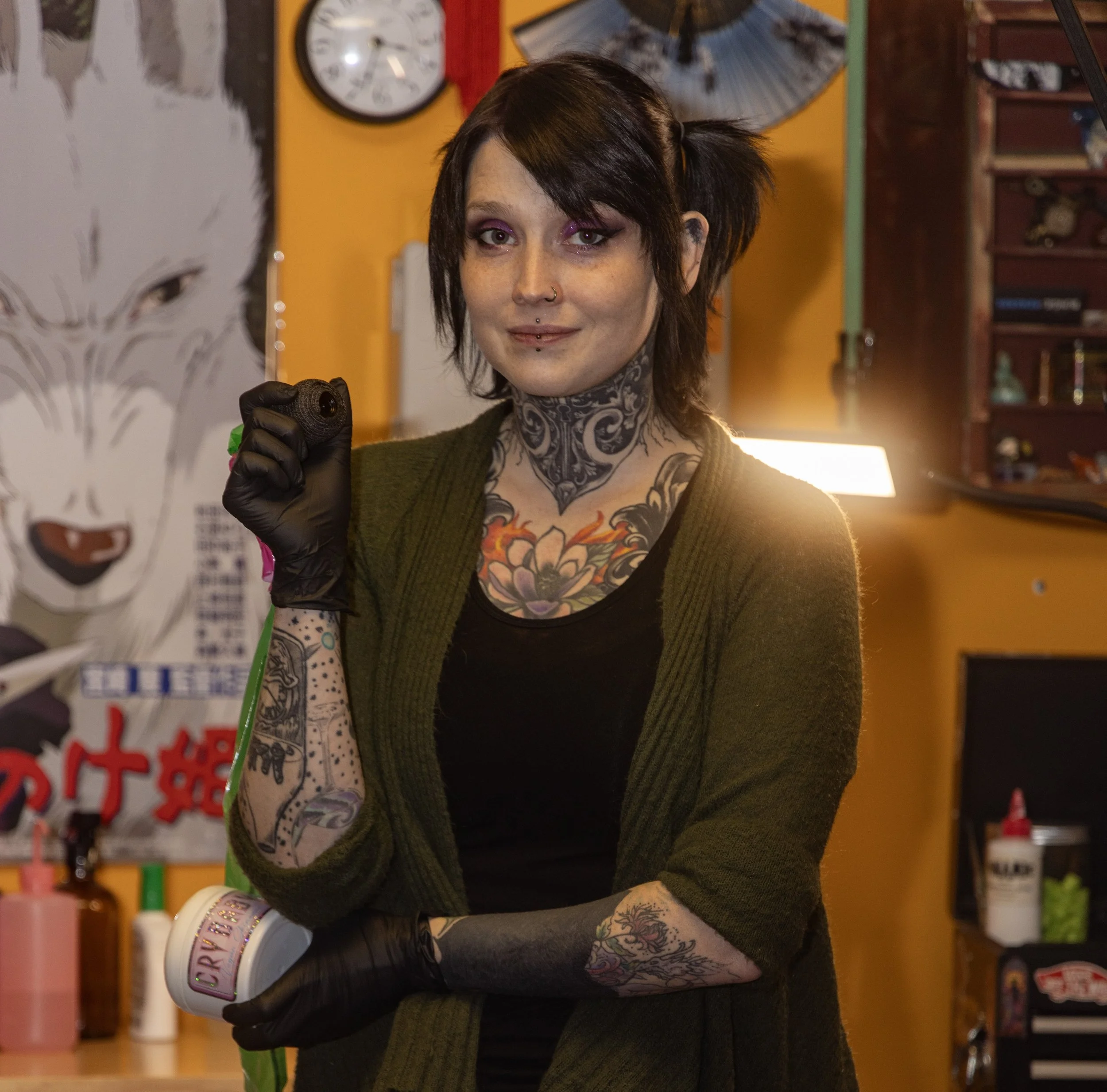 A photo of Capitol Fox (Caitlin), the lead artist and owner of Wicked Vibes Studio, holding a tattoo machine and Crybaby aftercare.