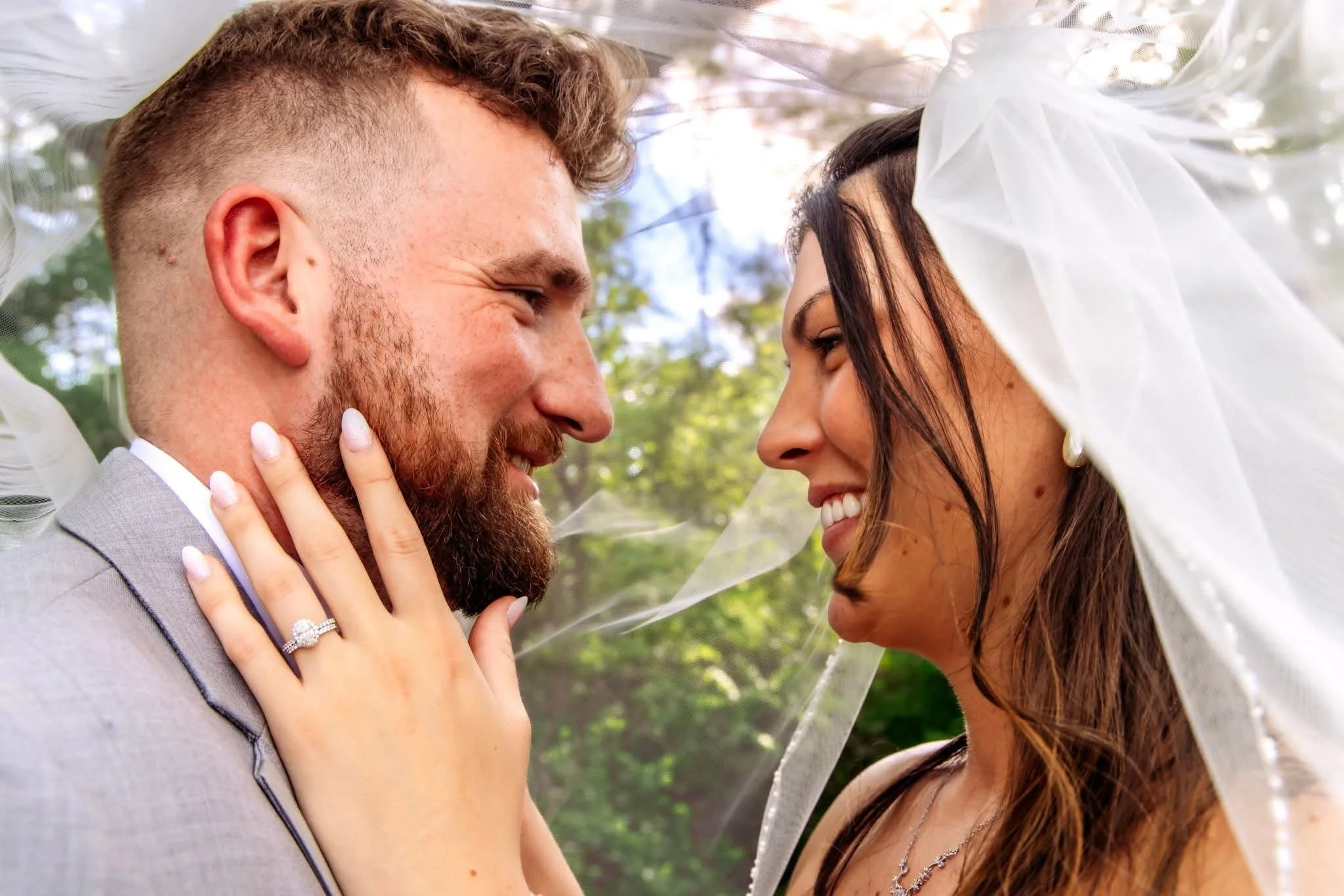 A husband and bride smile while looking into each other's eyes.