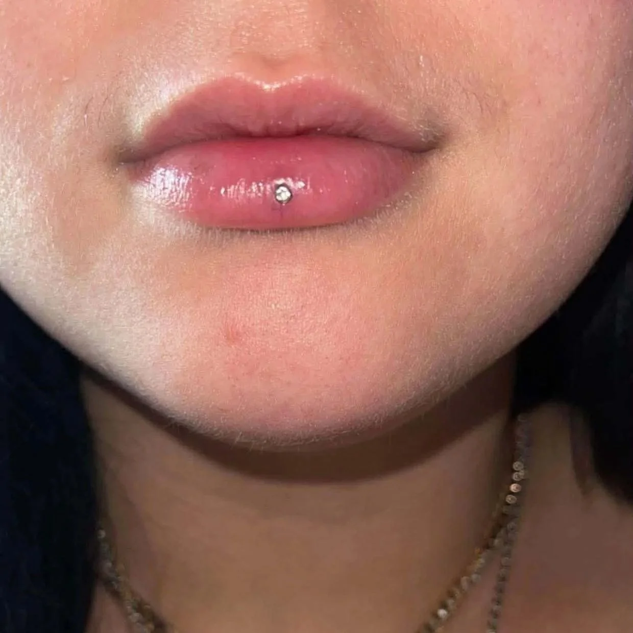 An upclose view of a woman's lip with a vertical lip piercing (Ashley).