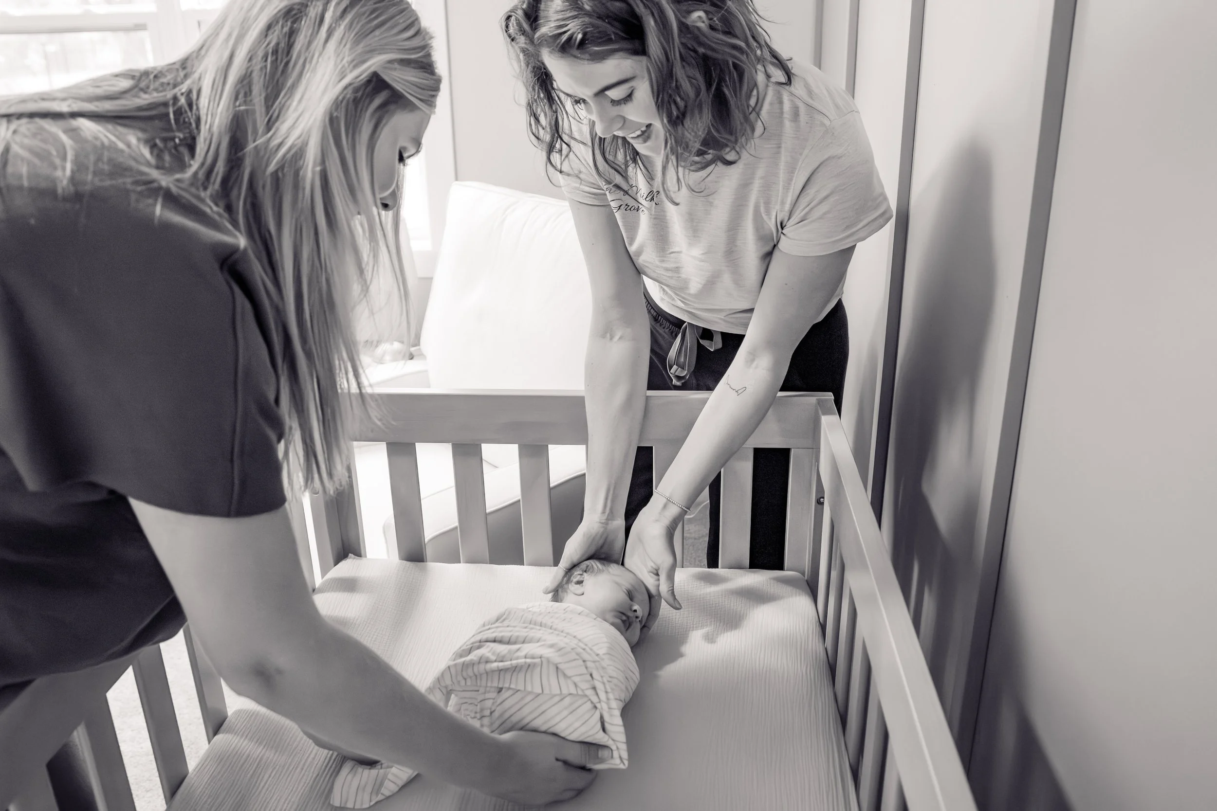 Two women gently caring for a sleeping baby in a crib.