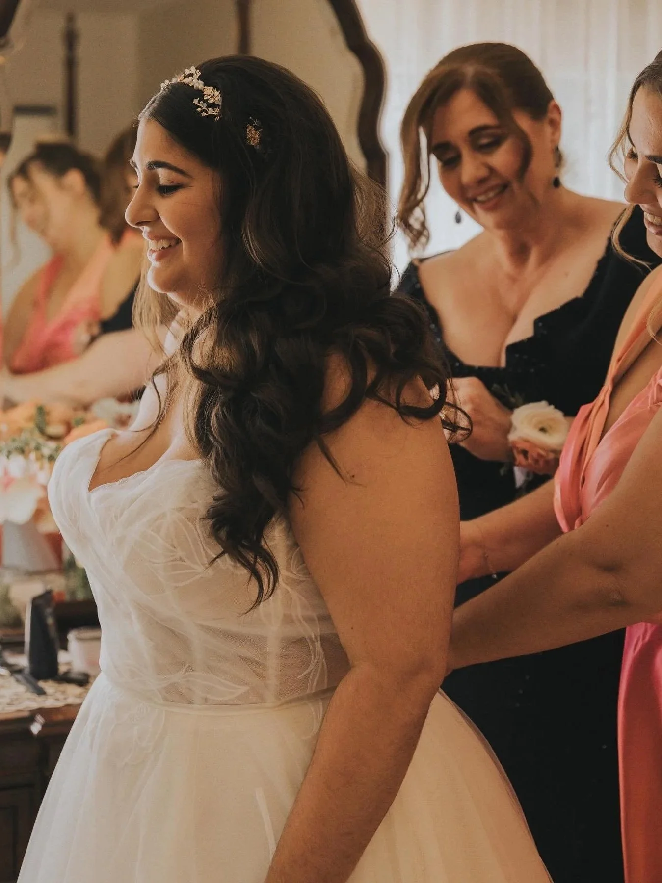 A bride in a white wedding dress getting ready, surrounded by women helping her with her dress.