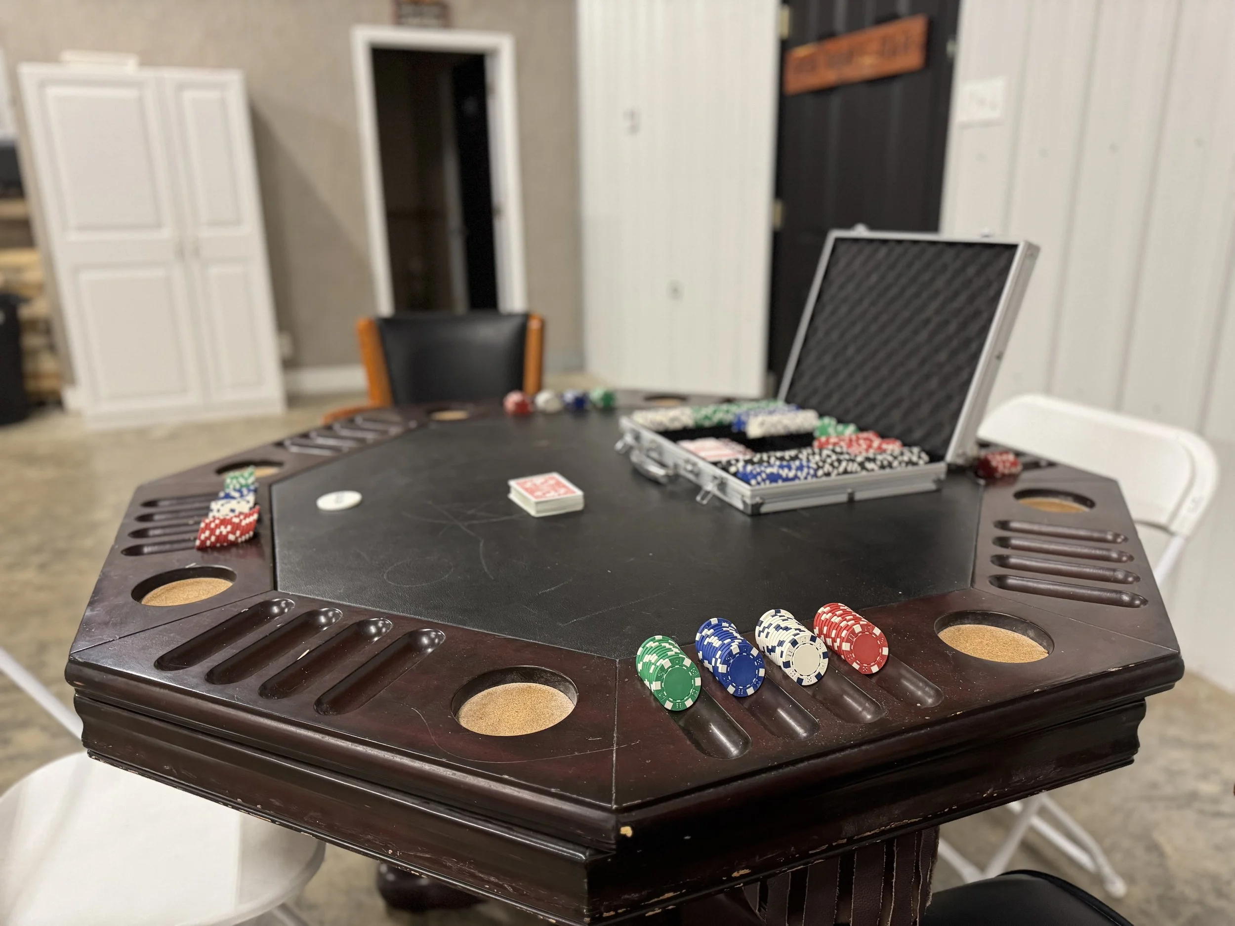 A poker table with chips and a deck of cards, surrounded by chairs in a game room setting.