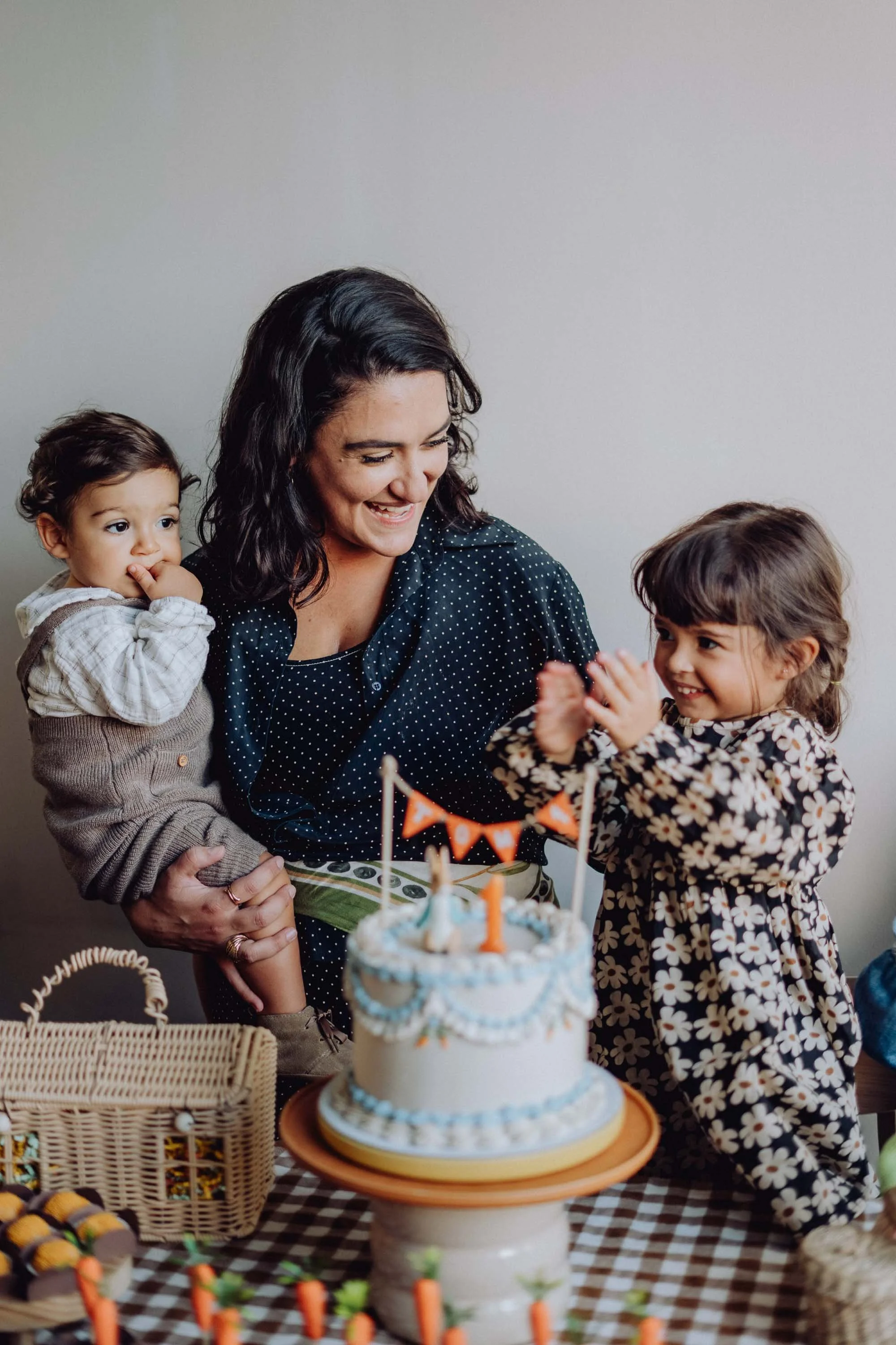 A woman celebrating a child's birthday with a cake, two children, and party decorations at a table.