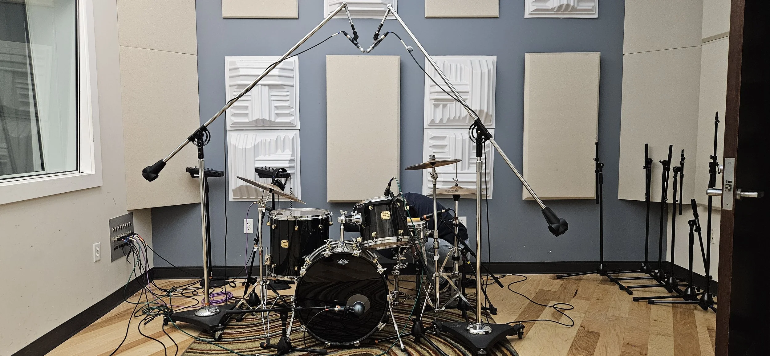 Music recording studio with a drum set, microphone, and soundproofing panels on the wall.
