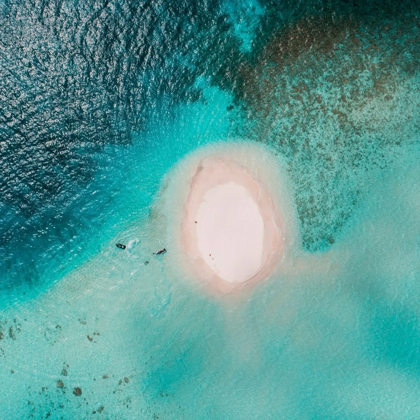 Aerial view of a small island with white sand surrounded by turquoise water and coral reefs.