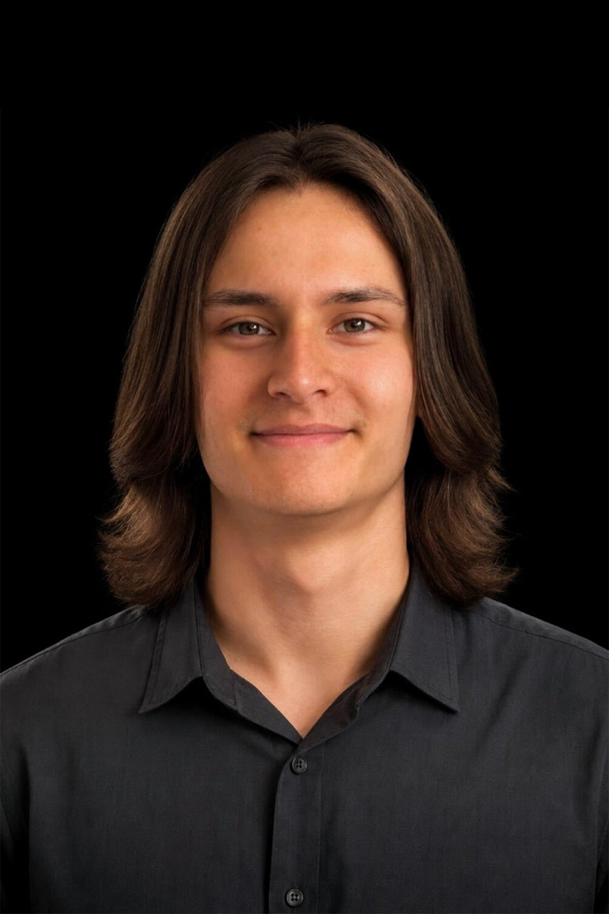 Portrait of a young man with shoulder-length brown hair, wearing a black button-up shirt, smiling against a black background.