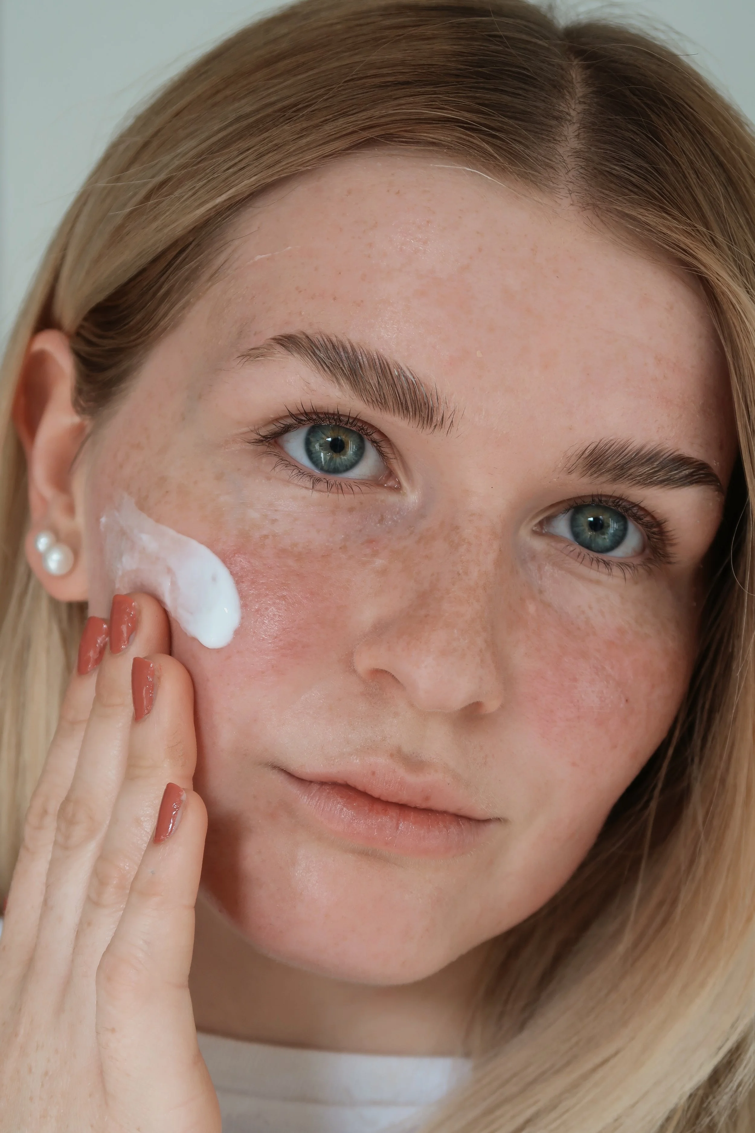 A woman with blue eyes and blonde hair applies Dr. SEA's superfood facial cream to her cheek.