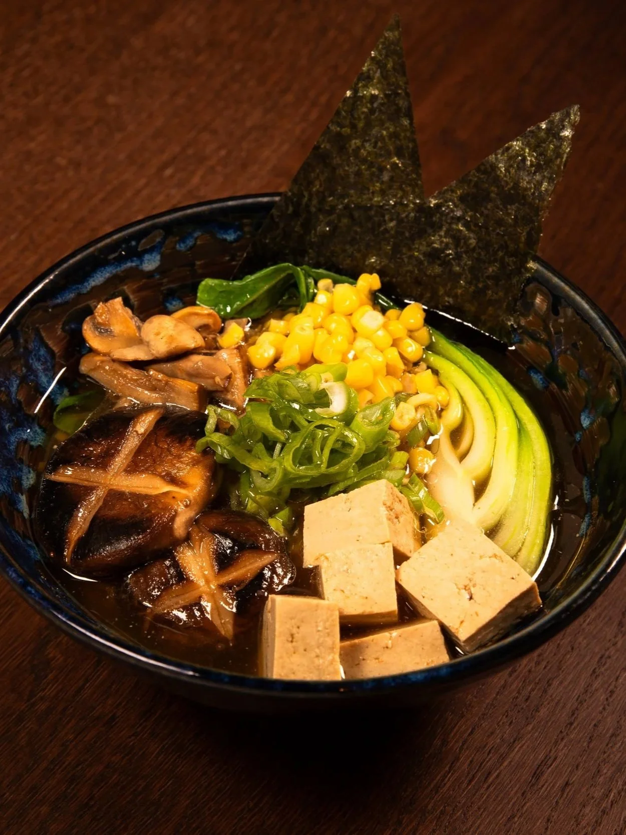 Schüssel mit Ramen-Nudeln, Tofu, grünen Zwiebeln, Mais, Algen, Pilzen und weiteren Zutaten.