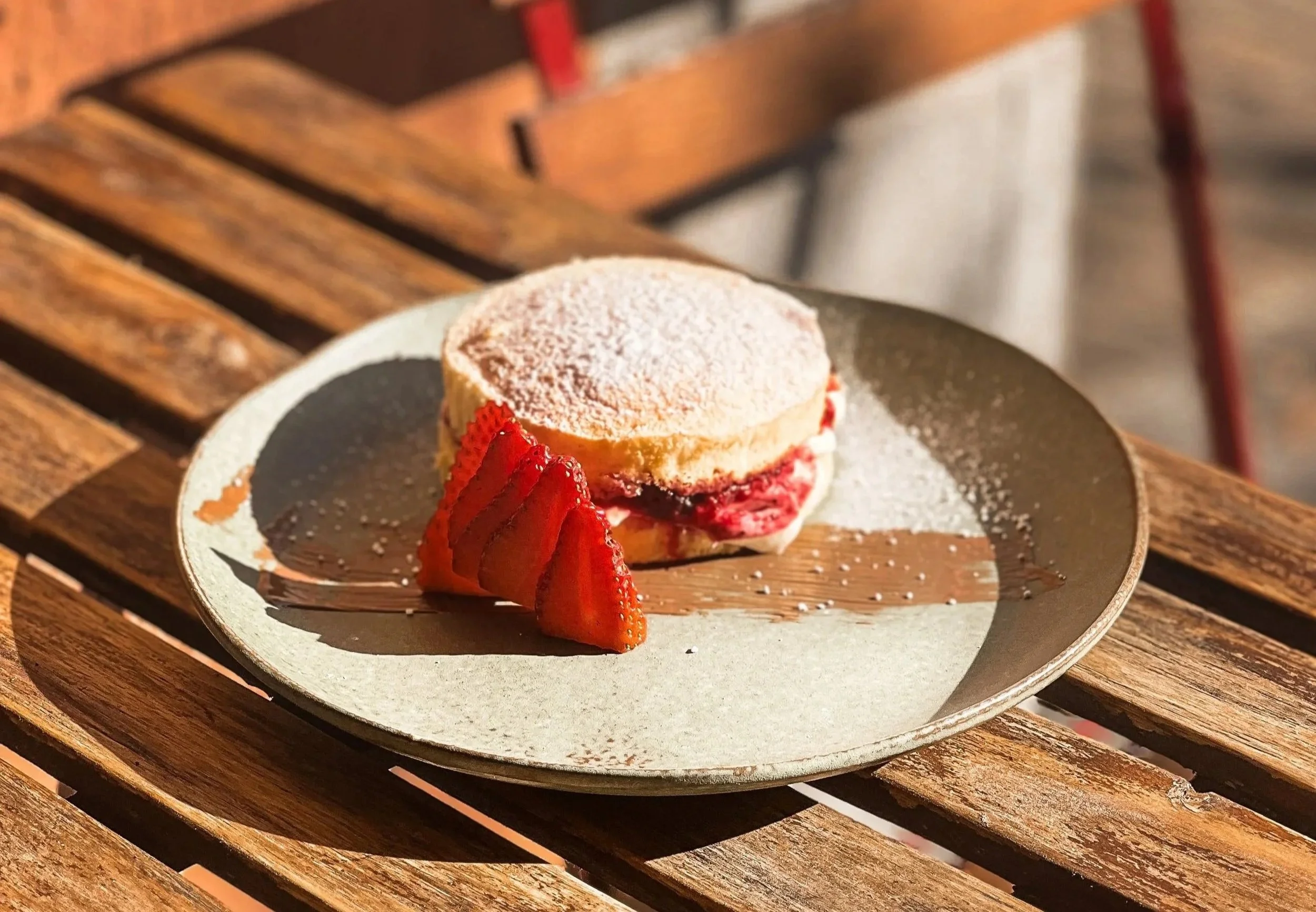 Ein Dessert mit Puderzucker, frischen Erdbeeren und einer Weißweincreme auf einem schwarzen Teller, auf einem Holztisch serviert.