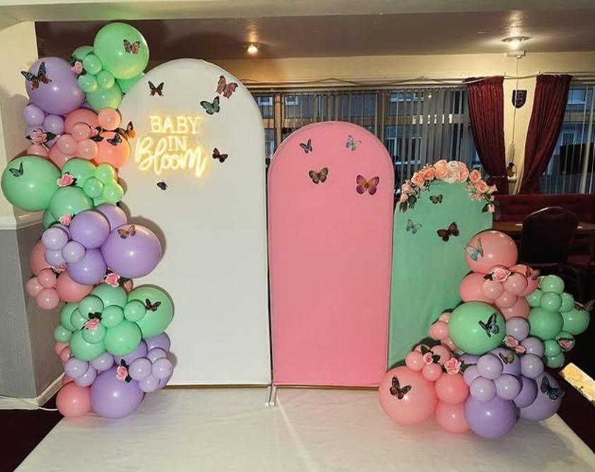 Decorative backdrop with pastel balloons and butterfly accents, with a sign that reads 'Baby in Bloom' for a baby shower or celebration.