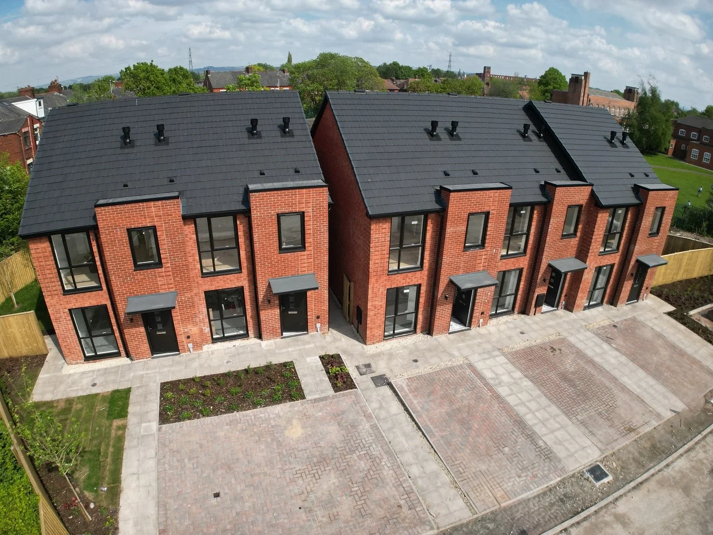 Aerial view of newly constructed brick townhouses with black roofs, large windows, and paved driveways in a residential neighborhood.
