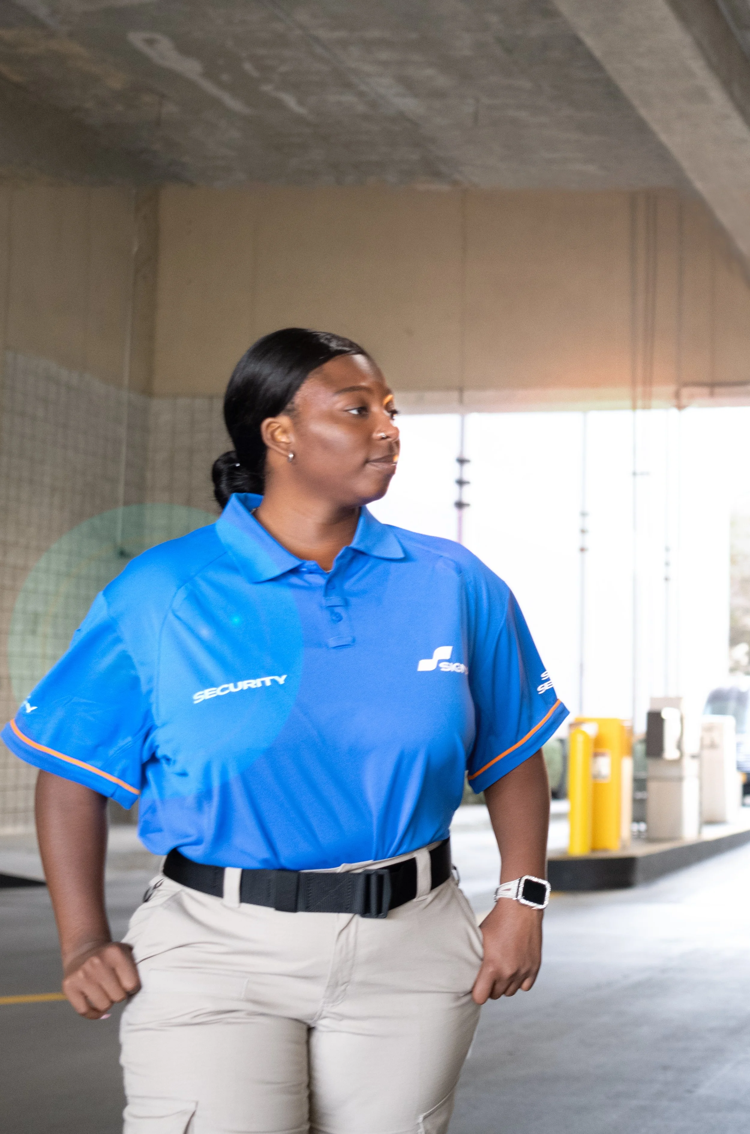 A security guard in uniform looking to the side in an indoor parking lot.