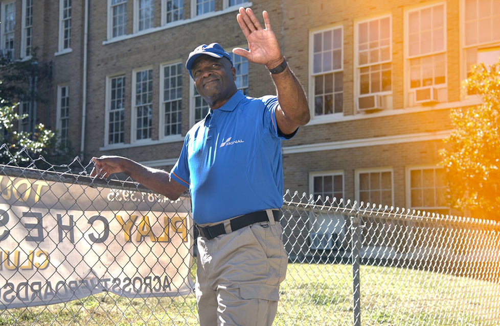 Line of parked cars along a city street with buildings and trees in the background.