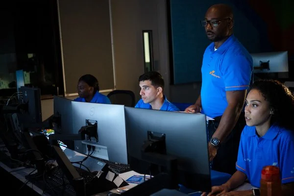 Remote monitoring team working on computers in a control room, dispatching security officers in the field.
