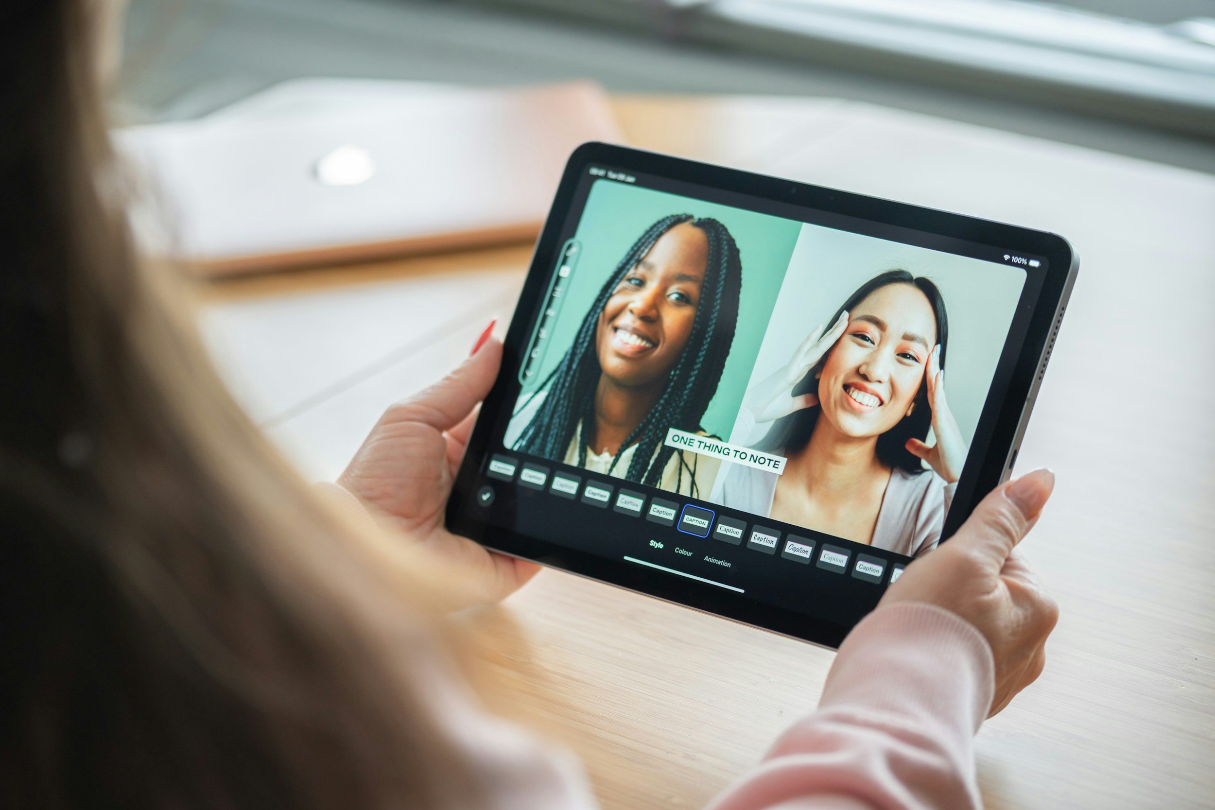 A person holding a tablet with a photo editing app open, showing two women smiling and posing for selfies.