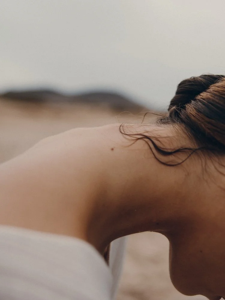 Close-up of a person's shoulder and neck, with brown hair visible and a blurred background.