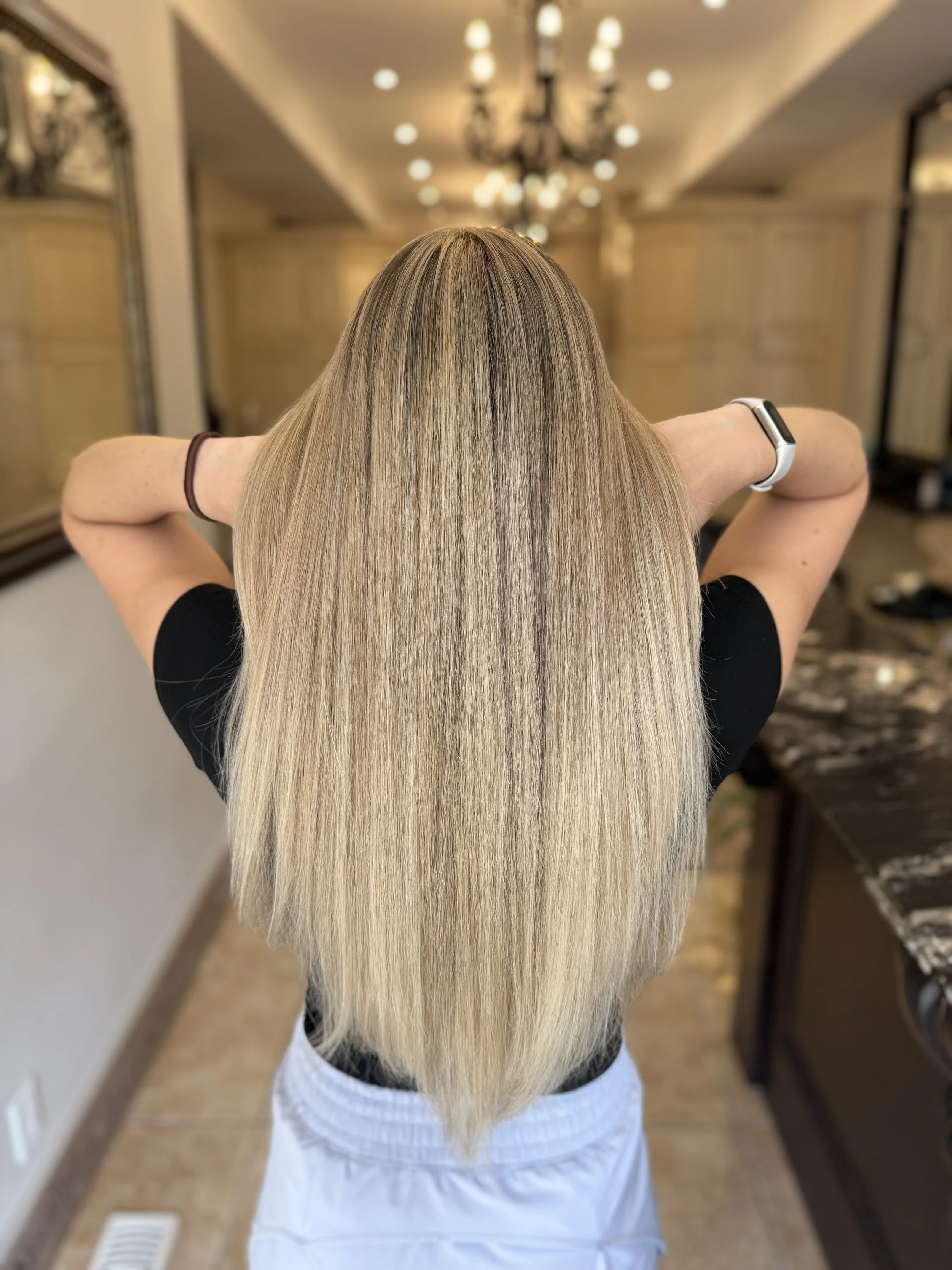 Back of a woman with long, wavy, silver-blonde hair in a salon setting.