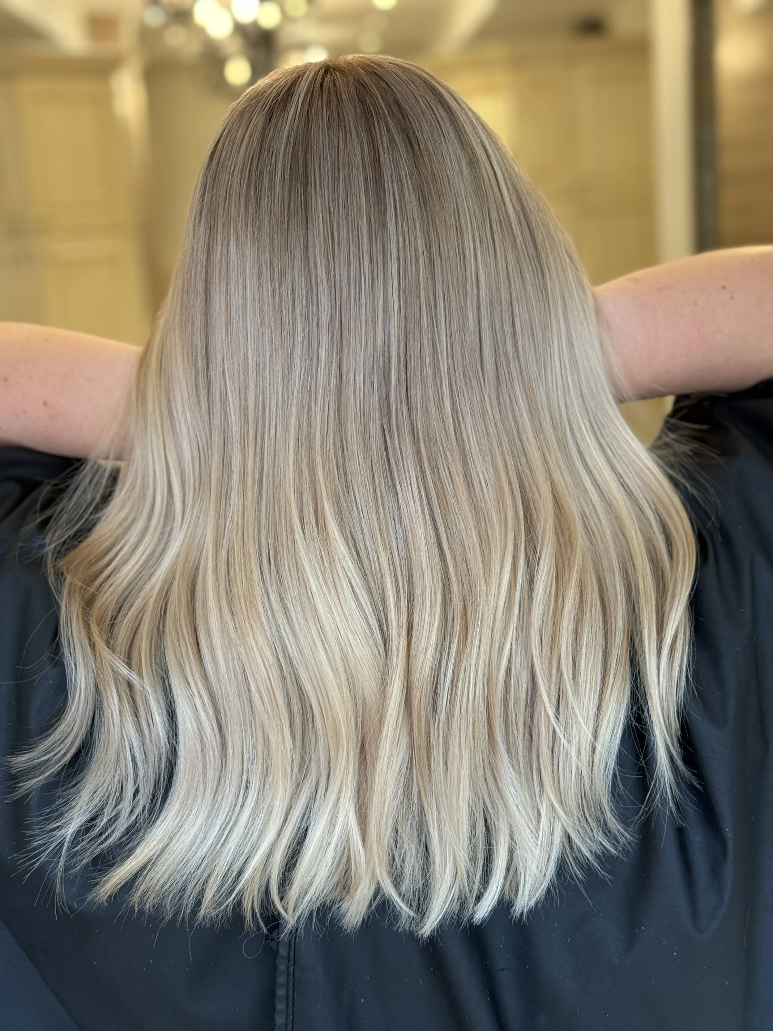 Back view of a woman with ash blonde hair styled in a messy half-up bun, wearing a white shirt.