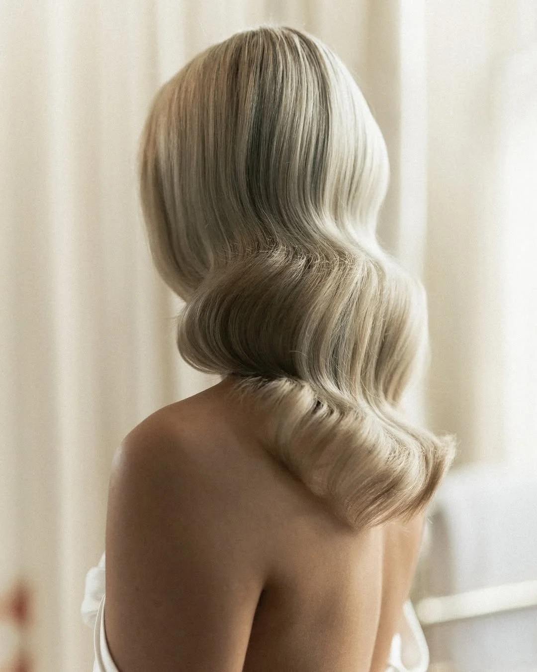 Back view of a woman with shoulder-length blonde hair styled in vintage Hollywood waves.