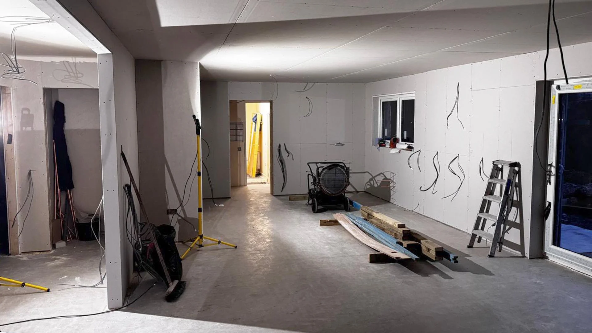 Interior of a house under construction with unfinished drywall, tools, wooden planks, and construction equipment scattered around.